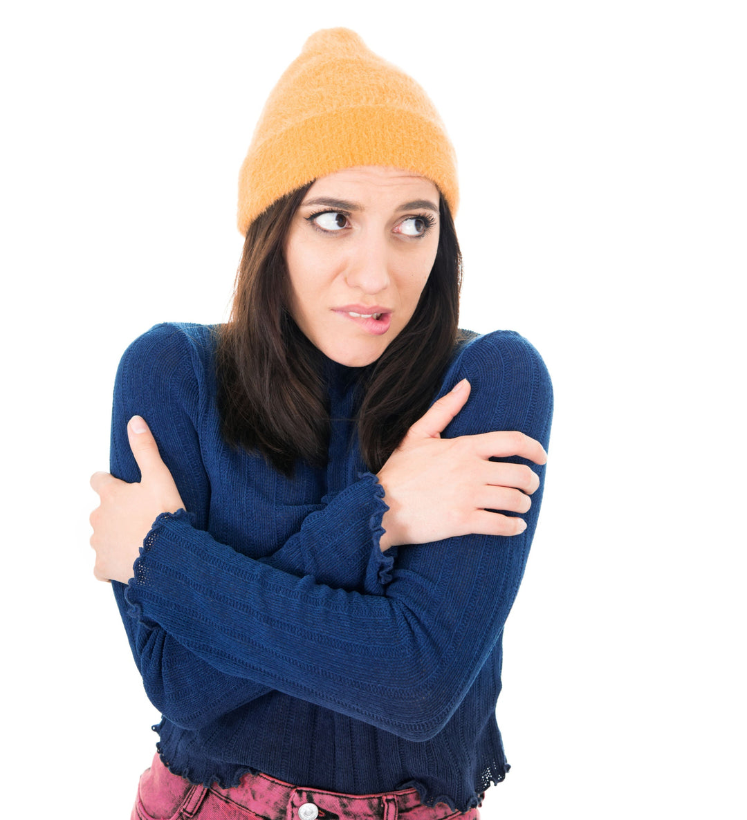 A woman wearing a hat and sweater is hugging  herself because she is cold
