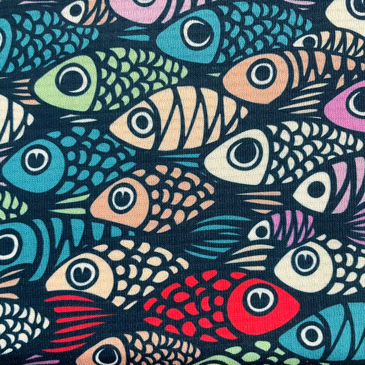 a close up image of the bucking the trend print of cartoon fish in multi colours with a red fish swimming in the opposite direction