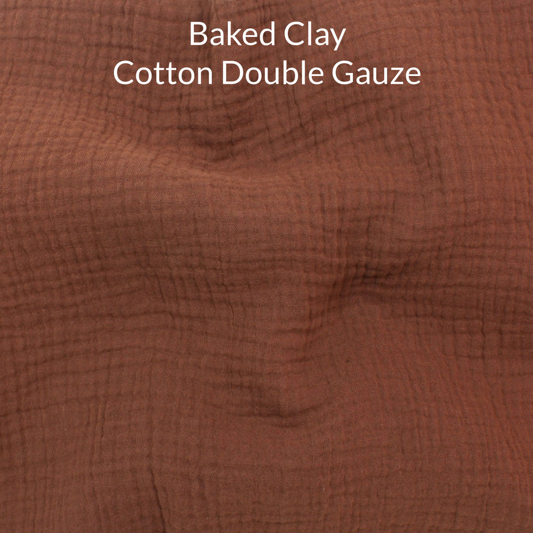 Close-up of a mid brown colored cotton double gauze fabric with text overlay noting the colour name is baked clay.