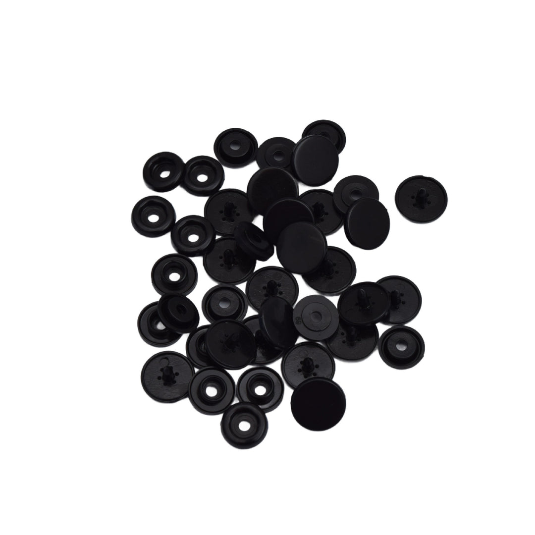 A pile of small black plastic snap component pieces, photographed on a plain white background.