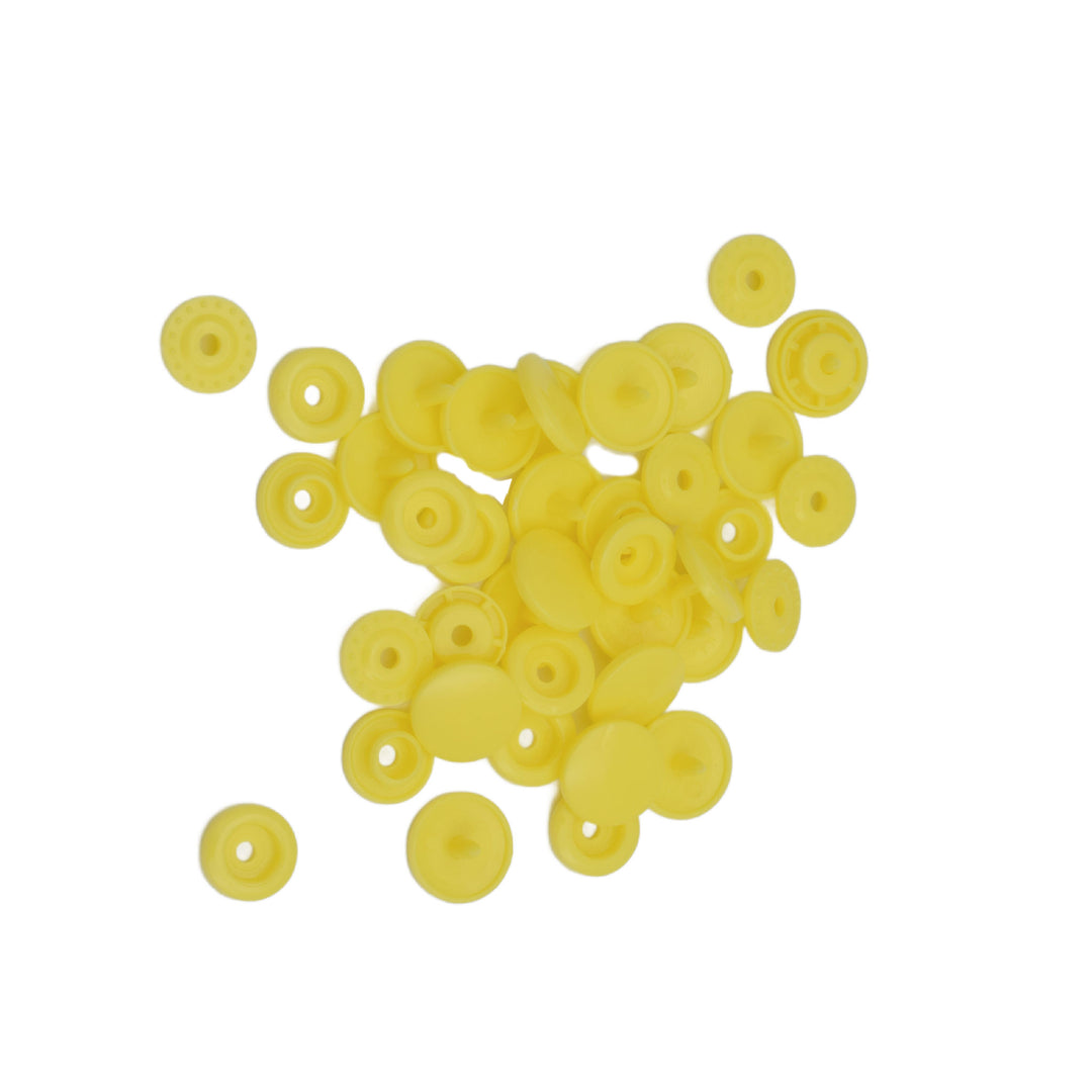 A pile of small round yellow plastic snap components, arranged on a plain white background.
