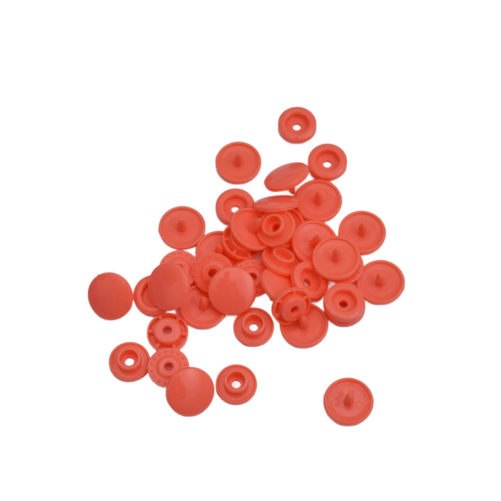 A pile of small round coral plastic snap components, scattered on a plain white background.