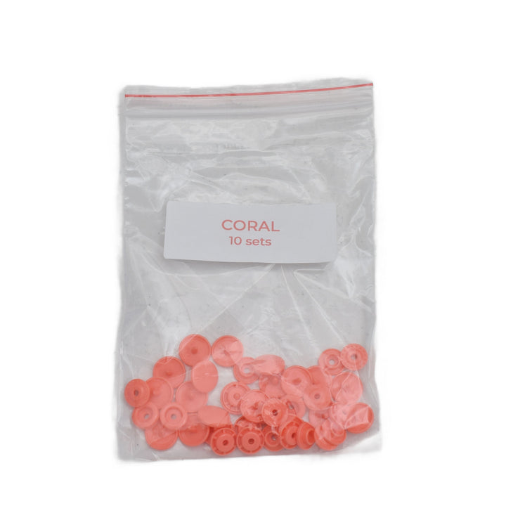 A clear plastic zip-top bag with a white label reading 'CORAL 10 sets' containing small coral-colored plastic snap pieces, shown on a white background.