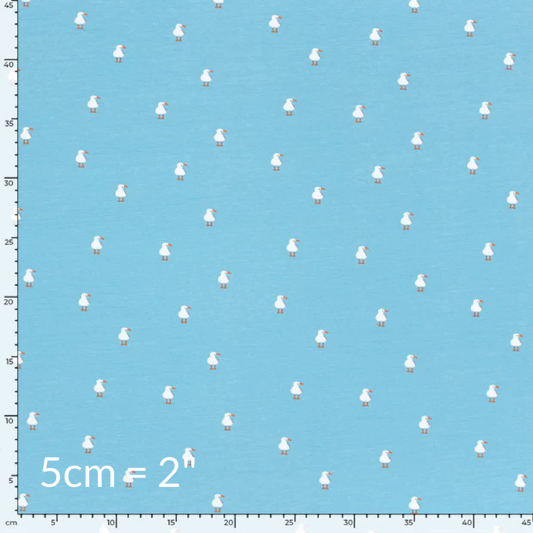 Fabric swatch showing cute children's print of white seagulls on a light blue background with ruler for scale
