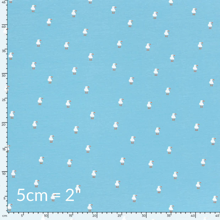 Fabric swatch showing cute children's print of white seagulls on a light blue background with ruler for scale
