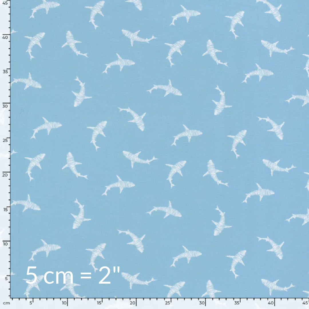 Fabric swatch showing cute children's print of white sharks on a light blue background with ruler for scale