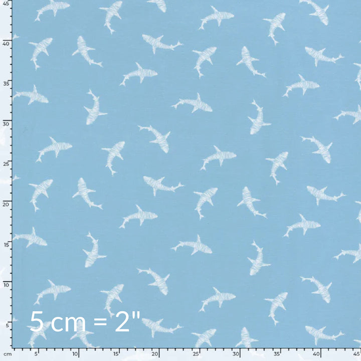 Fabric swatch showing cute children's print of white sharks on a light blue background with ruler for scale