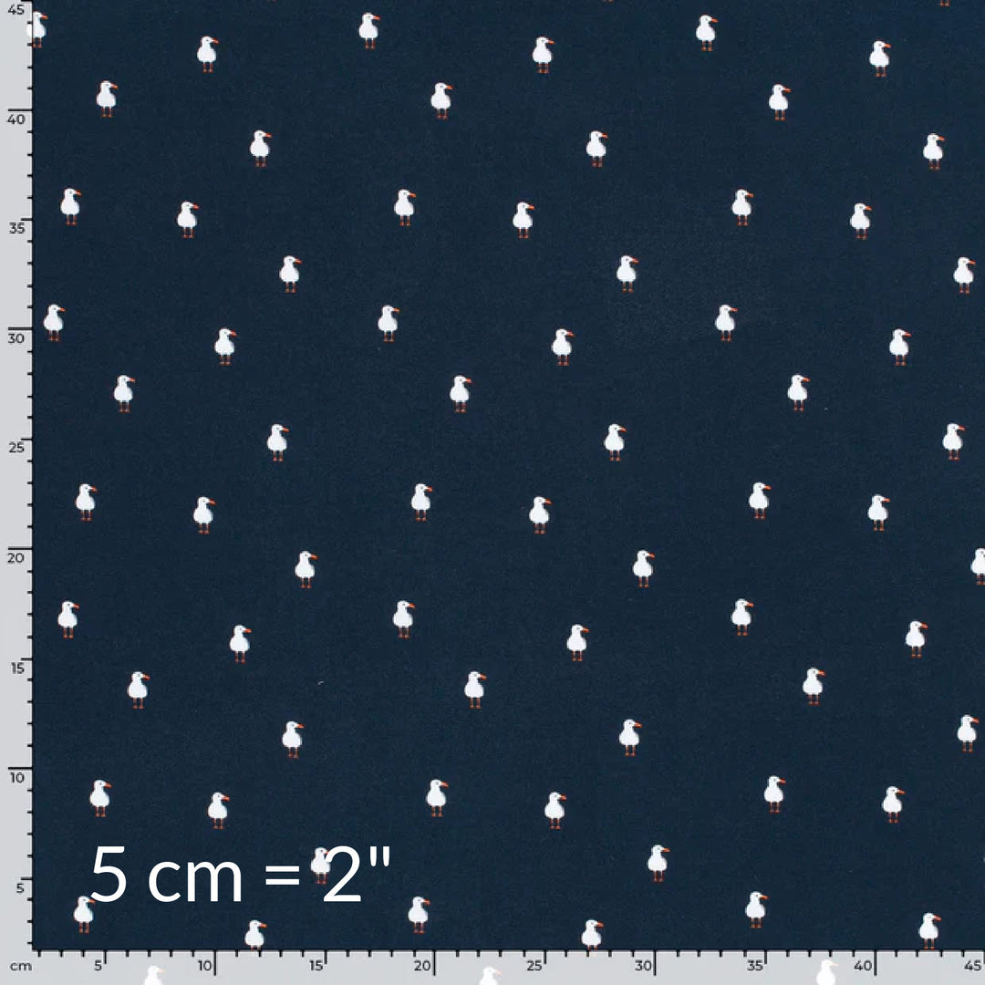 Fabric swatch showing cute children's print of white seagulls on a navy background with ruler for scale