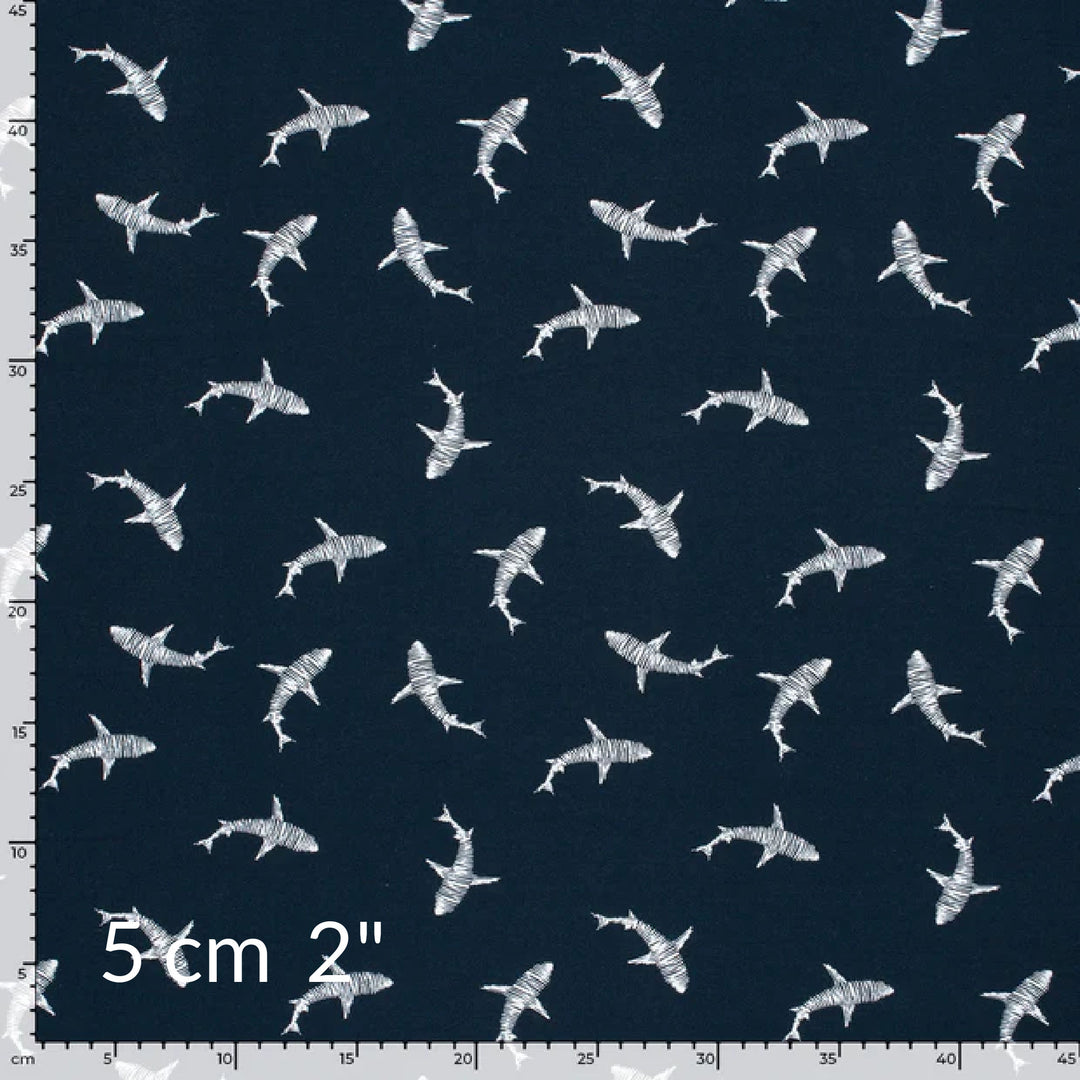 Fabric swatch showing cute children's print of white sharks on a navy background with ruler for scale