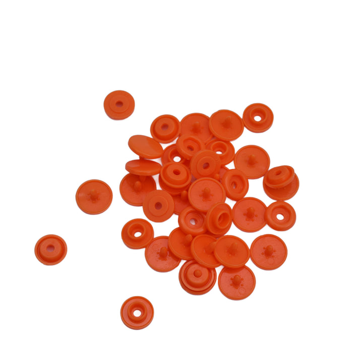 A pile of small orange plastic snap components, scattered on a plain white background.