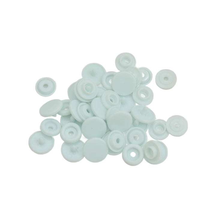 A pile of small, round, pale blue plastic snap component pieces, arranged on a solid white background.