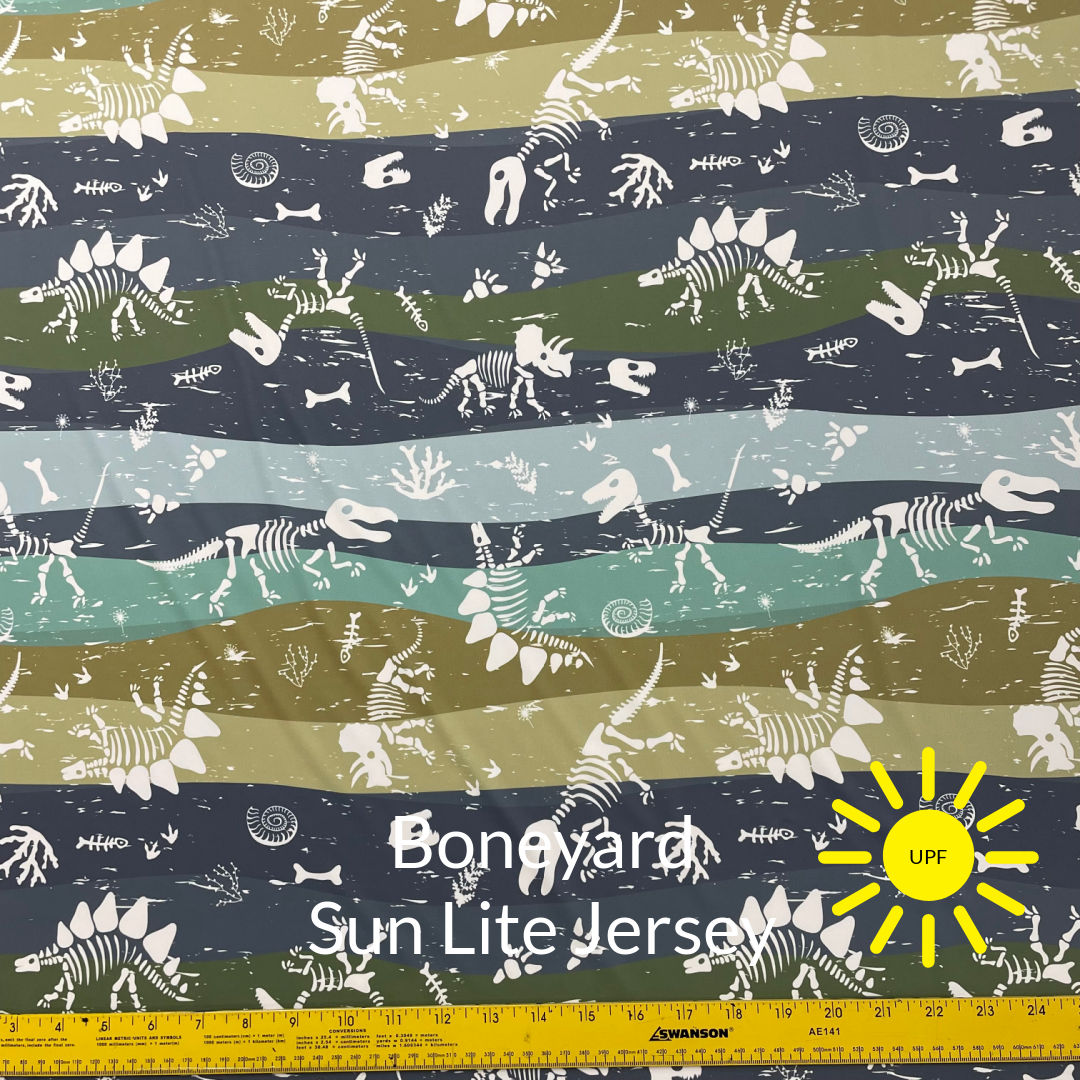 Boneyard Sun Lite Jersey Fabric with white dinosaur skeleton drawings on wavy striped background in beige grey pale blue olive green and khaki